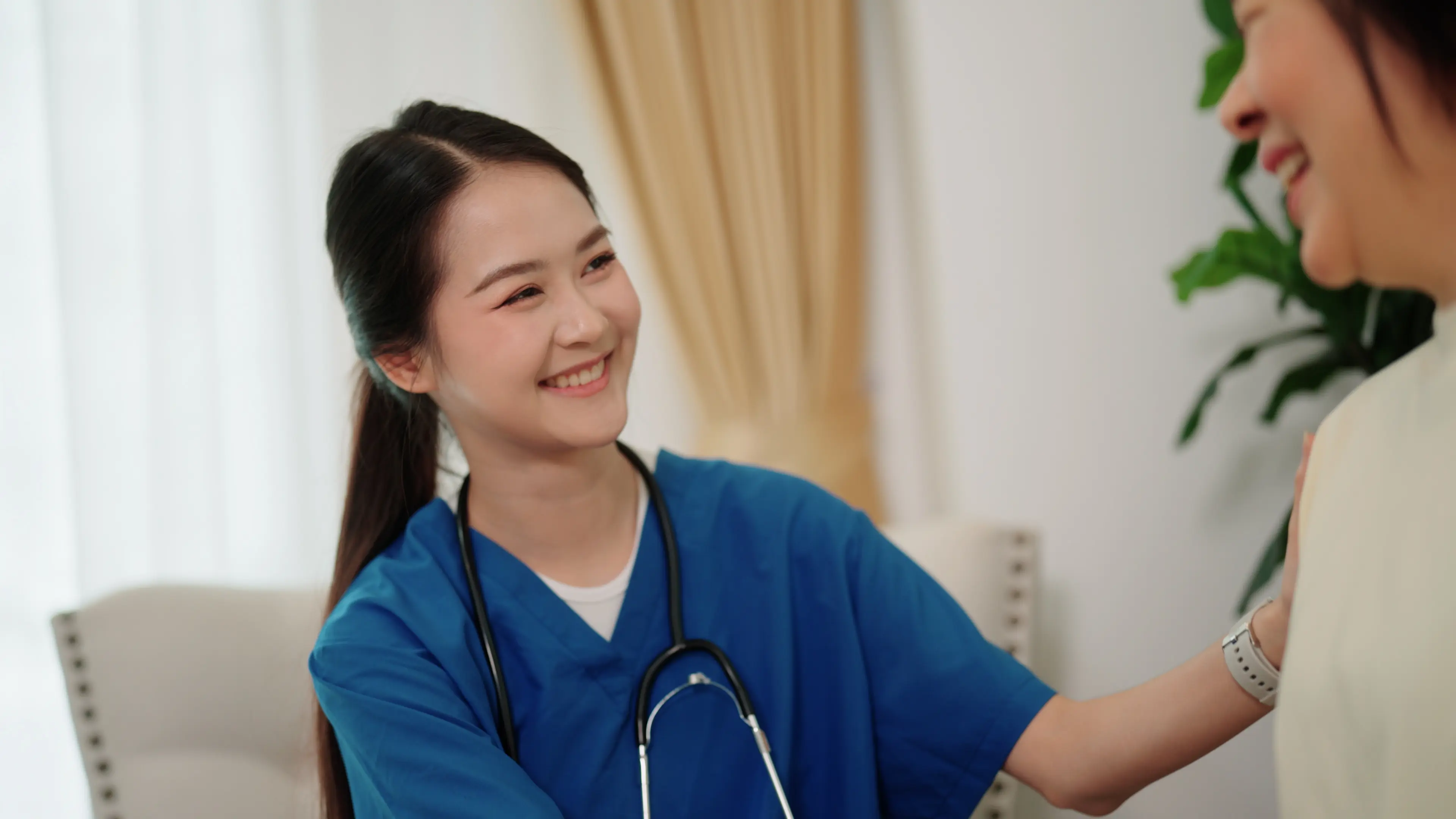 Female doctor offering emotional support to an elderly woman patient by holding her hand and gently placing a hand on her shoulder.